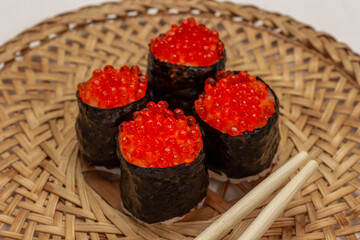 Nori maki with caviar and chopsticks on wicker plate.