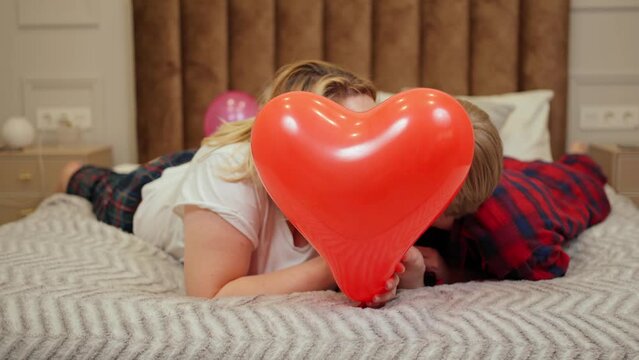 two women in love kiss and hide behind heart-shaped balloons in bed. love. valentine's day lgbt couple
