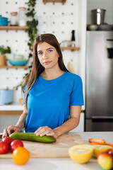 Young woman preparing salad in the kitchen and looking at camera