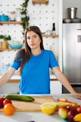 Young woman preparing salad in the kitchen and looking at camera