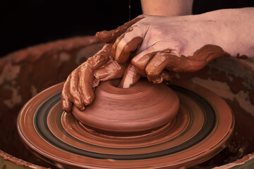 Potter's hands while working on a potter's wheel. A lump of red clay turns into a pot. The process of forming a ceramic product