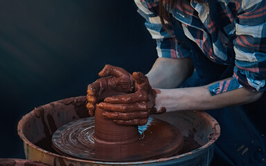 The girl potters on the wheel. Thin strong hands act confidently with clay. The process of forming...