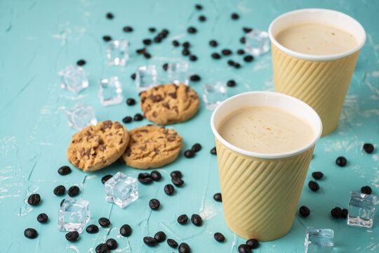 Top view of two cardboard cups with cappuccino coffee on blue table with coffee beans and cookies, horizontal