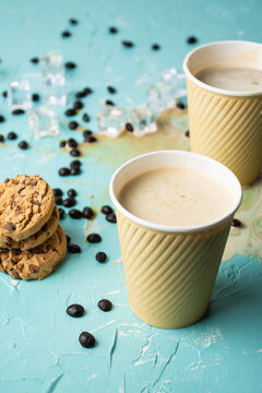 Top view of two cardboard cups with cappuccino coffee on blue table, spilled coffee, coffee beans and cookies, vertical