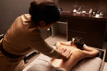 Rear view of a masseuse gives a body massage to a young woman. Spa relaxation concept.