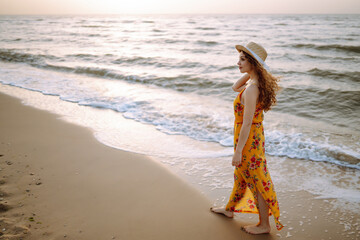Fototapeta na wymiar Beautiful woman in summer dress and hat walking on the beach. Travel, weekend, relax and lifestyle concept.