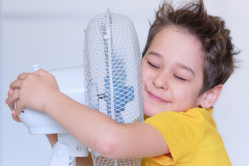 preschool boy cooling in front of fan. Little child refreshing from heat in front of small fan at...