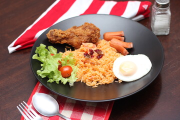 American fried rice served with sausages, cucumbers, shredded vegetables in a gray plate on a white table with seasoning.