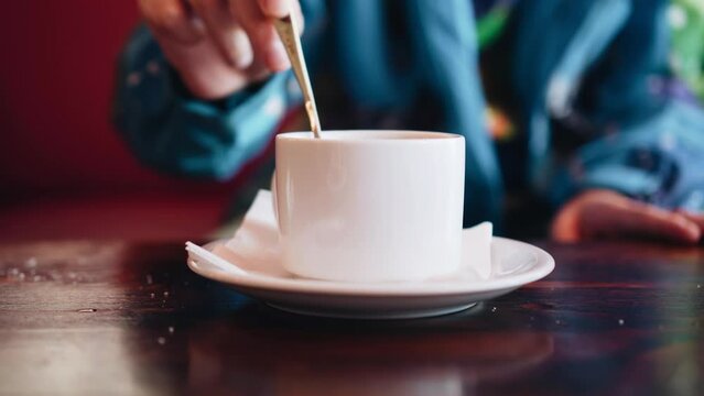 The guy is stirring sugar in a white cup of coffee. Close-up shooting