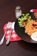 American fried rice served with sausages, cucumbers, shredded vegetables in a gray plate on a white table with seasoning.