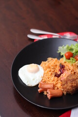 American fried rice served with sausages, cucumbers, shredded vegetables in a gray plate on a white table with seasoning.