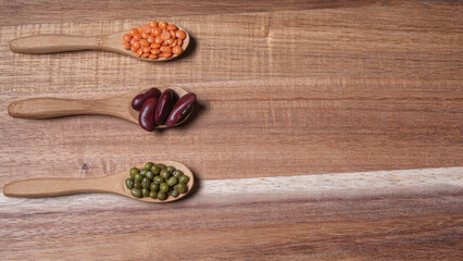 Three wooden spoons with legumes of different types: beans, red lentils and soybeans