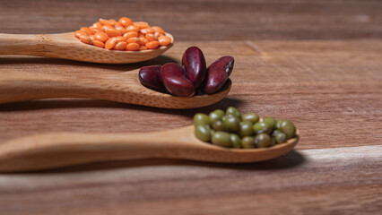 Three wooden spoons with legumes of different types: beans, red lentils and soybeans