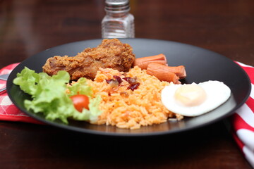 American fried rice served with sausages, cucumbers, shredded vegetables in a gray plate on a white table with seasoning.