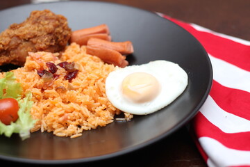 American fried rice served with sausages, cucumbers, shredded vegetables in a gray plate on a white table with seasoning.