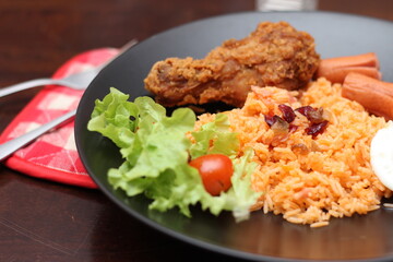 American fried rice served with sausages, cucumbers, shredded vegetables in a gray plate on a white table with seasoning.