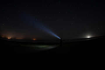 Adventurous man watching the stars on a beach at night with his headlamp shinning up at the stars.