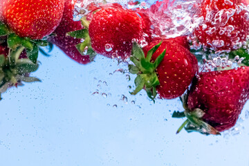 Strawberries in water with water splash and air bubbles on blue background. Close up image.