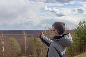A teenage boy takes pictures on a smartphone of the landscape of a swamp in spring or autumn