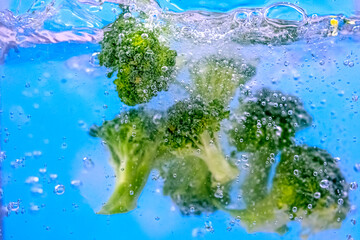 Fresh broccoli slices in water with air bubbles on blue background. Boiling water with fresh vegetables, close-up