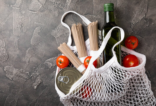 Ecobag with a grocery set. White string bag, shopper. Buckwheat sobo, cherry tomatoes, olive oil and canned meat. Shopping concept. Healthy food. Purchases. - Powered by Adobe