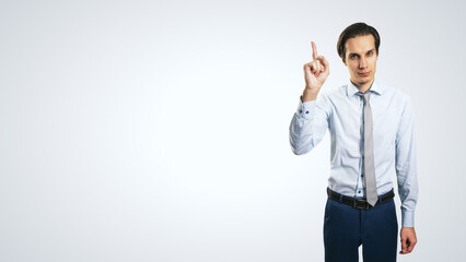 Young handsome man in shirt with raising up hand and forefinger isolated on abstract light grey background with empty place for your logo or text, mock up