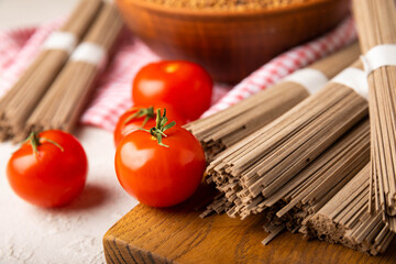 Buckwheat pasta with cherry tomatoes on a black textured marble background. Raw pasta. Ingredients for a gluten free dish. Healthy food. Place to copy.