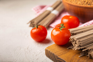 Buckwheat pasta with cherry tomatoes on a black textured marble background. Raw pasta. Ingredients for a gluten free dish. Healthy food. Place to copy.