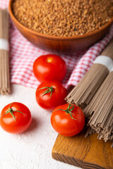 Buckwheat pasta with cherry tomatoes on a black textured marble background. Raw pasta. Ingredients for a gluten free dish. Healthy food. Place to copy.