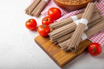 Buckwheat pasta with cherry tomatoes on a black textured marble background. Raw pasta. Ingredients for a gluten free dish. Healthy food. Place to copy.