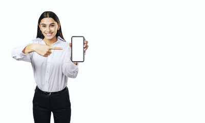 Mobile application concept with smiling businesswoman in white shirt showing modern smartphone with blank white screen isolated on light background with place for your logo or text, mock up