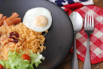 American fried rice served with sausages, cucumbers, shredded vegetables in a gray plate on a white table with seasoning.