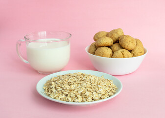 Oatmeal, the oatmeal liver in a white bowl, a transparent glass of milk on a pink background, a side view, the concept of healthy eating and cooking cereal or cookies. High-quality photo