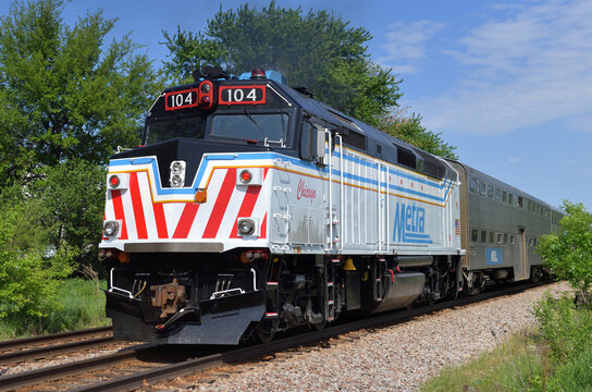 A Metra commuter train after departing the local train station on a spring day being pushed on its journey to Chicago. The locomotive has a special paint scheme that honors the City of Chicago.