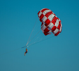 Perissa, Greece - July 13 2019:   Two people hang from a parachute, paragliding over the waters of the Aegeean Sea off the Perissa seafront