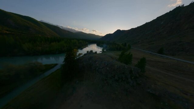 Aerial view flight over darkness river water surface with stones and grass forest trees and mountain valley sunset. FPV sports drone shot evening night cliff scenery environment highway empty road 4k