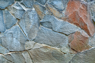 Natural granite stone wall background. Granite - rock stone wall texture. Exterior wall of decorative broken stone in blue-grey - orange colors. Building industry concept