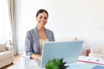 Smiling young woman using laptop at home, looking at screen, chatting, wearing wireless headset having video conference . business trainer tutoring by webcam, online training, e-coaching concept