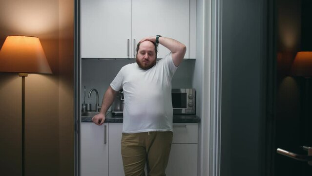 Portrait of frustrated overweight man stand in small kitchen