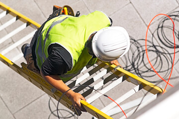 electrician worker on staircase installing optical fiber cable for internet and telephone lines in...
