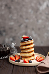 Fresh pancakes laid out in a stack, decorated with fresh berries, sprinkled with powdered sugar, beautiful serving