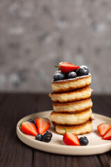 Fresh pancakes laid out in a stack, decorated with fresh berries, sprinkled with powdered sugar, beautiful serving