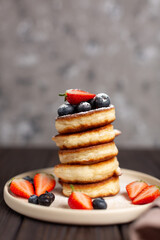 Fresh pancakes laid out in a stack, decorated with fresh berries, sprinkled with powdered sugar, beautiful serving