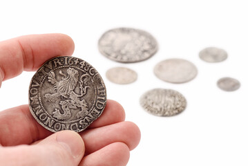 Old silver thaler in male hand and coins on white background. Lion Daalder. Selective focus.