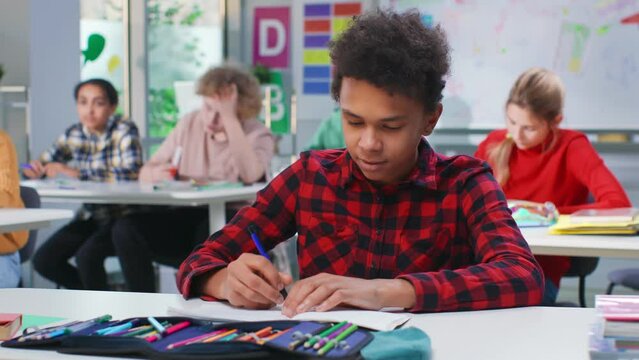 African-American teen student write in notebook at lesson in classroom