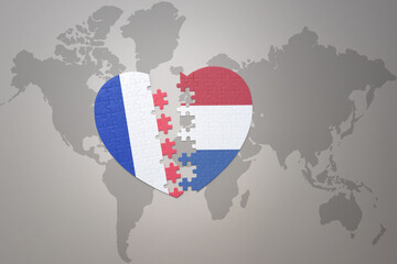 puzzle heart with the national flag of france and netherlands on a world map background. Concept.