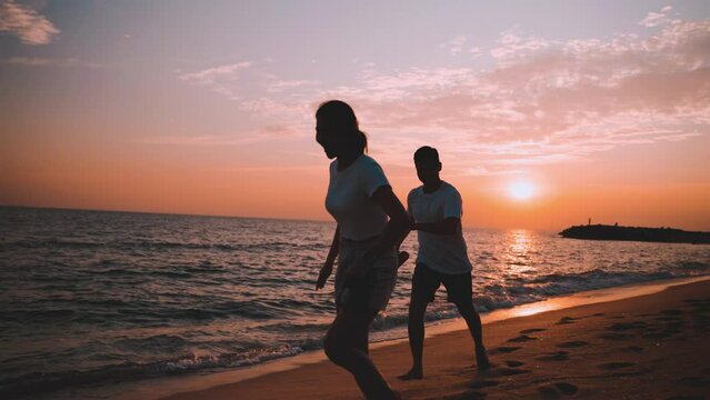 Happy Asian couple jogging and running with tease together on beach while beauty in nature of sunset time evening of vacation summer. Young in love romantic and relaxing at seaside. Honeymoon concept.
