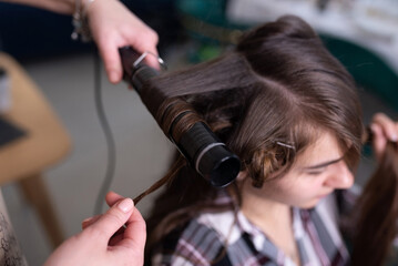 The stylist curls the girl's hair with a curling iron