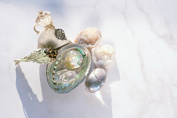 Quartz crystals, white sage bundle, abalone sea shell, witch bag on light marble background....