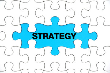 Fototapeta premium The word STRATEGY on the blanks of the White jigsaw puzzle on blue background. Success Concepts and Strategies. 